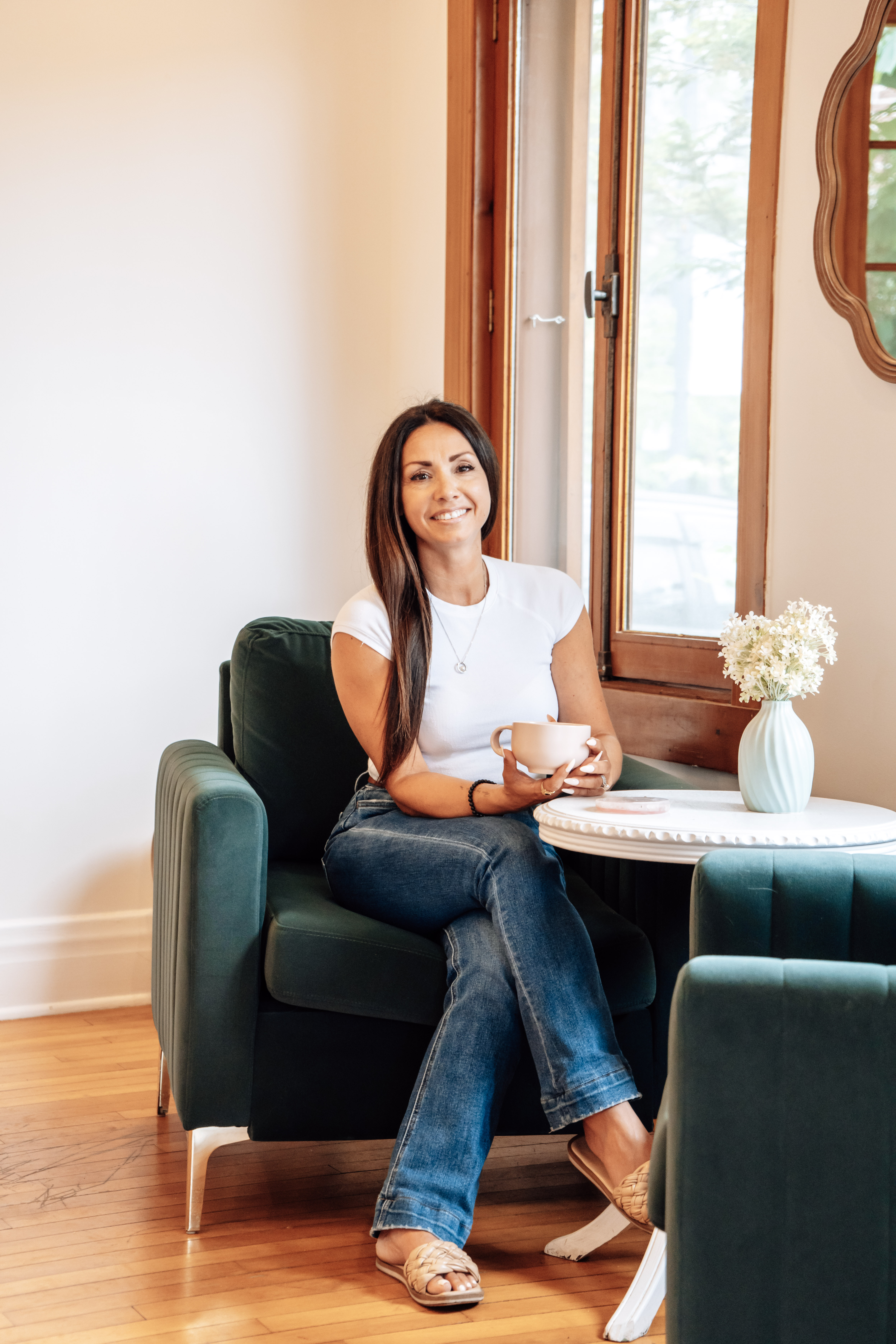 Shanna Giannakis seated in a dark green chair holding a coffee cup